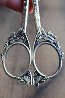 Butterfly Scissors in Antique Gold Finish on blurred background.