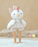 Stuffed Claire toy chicken in a floral outfit with a bow on a soft surface