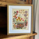 Dreaming of Summer Cross Stitch framed design of a house surrounded by flowers.