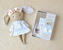 Stuffed bunny Jeanne doll with a floral dress next to a sewing kit on a wooden surface