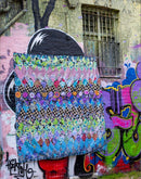 A design from the book Kaffe Fassett's Quilts in London showing colorful a quilt with floral fabric in a diamond pattern hanging against a graffiti-covered wall.