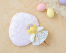Toy Mini Robine Chick Doll Kit with a floral dress and purple bow on a wooden surface with pastel-colored eggs.