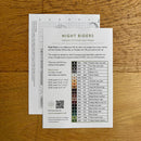 Cross stitch pattern chart and back cover titled 'Night Riders' on a wooden surface