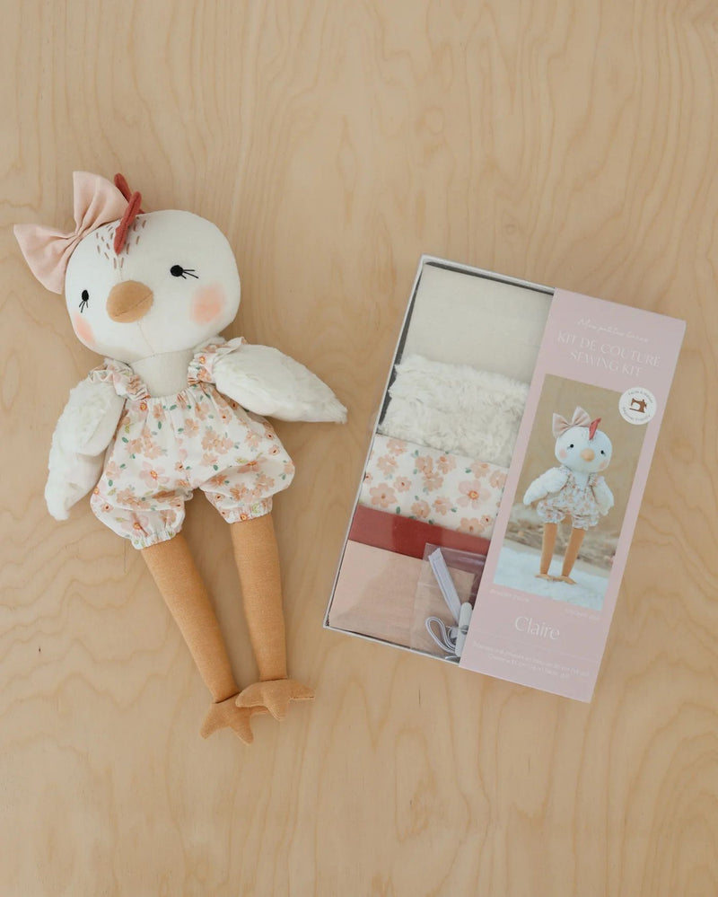 Stuffed Claire toy chicken with floral outfit next to kit packaging on a wooden surface