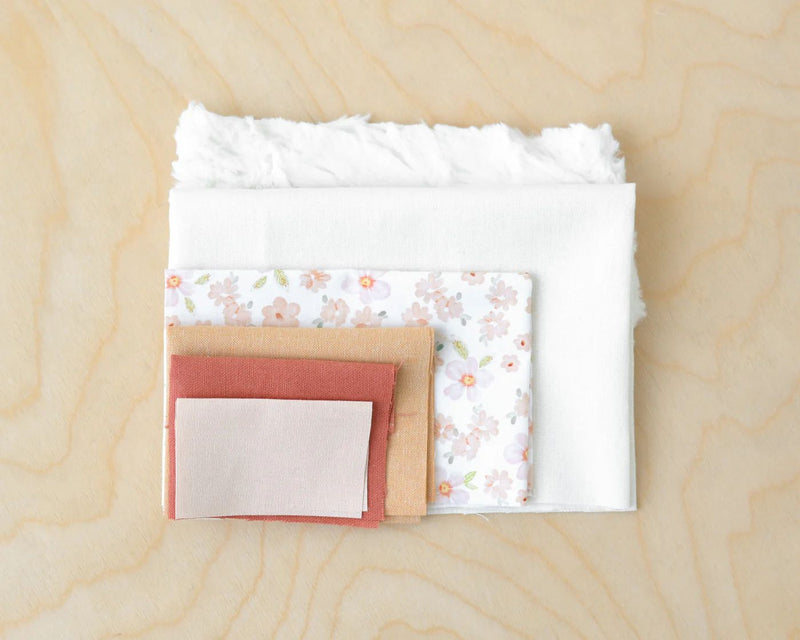 Stack of fabric swatches used for Claire doll kit on a wooden surface