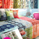 Color Blocks Free PDF Quilt Pattern quilt with patterned pillows on a bed in a room with fabric rolls in the background.