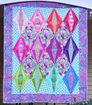 Crown Jewels Free PDF Quilt Pattern shows Colorful diamond patterned quilt on a stand outdoors.