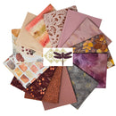 Desert Blooms and Friends Fat Quarter Bundle shows a fan arrangement of multiple patterned fabric fat quarters in muted autumn and floral tones, including dusty pink, mauve, burgundy, brown, cream, and yellow-gold motifs, with a dragonfly logo centered over the pile on a white background.
