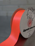 A close-up of a spool of bright orange satin ribbon with a white label reading 'Supreme Laces Inc.' on a dark surface. Double-Face Satin Ribbon 38mm (1.5") Wide