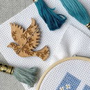 Wooden dove-shaped needle minder on aida cloth with embroidery floss.