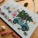 Driving Home for Christmas cross-stitch design of a vintage truck with a Christmas tree placed on a wooden surface