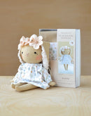 Handmade Jeanne doll with floral headband and dress next to a sewing kit packaging on a wooden surface.