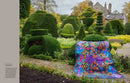 A colorful quiltt is draped over a chair in a landscaped garden with neatly trimmed topiary hedges and stone buildings in the background from the book, Kaffe Fassett's Quilts at an English Manor House.