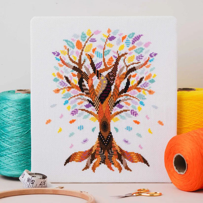 Mandala Tree Cross Stitch design upright on table top surrounded by thread, scissors, and hoop.