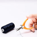 Hand holding Multi-Purpose Handy Cut orange scissors with a spool of black thread on a white background