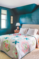 Pattern from "Not Your Typical Jelly Roll Quilts" shows bedroom with teal walls, a colorful quilt on a bed, and a lamp.