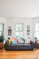 Pattern from "Not Your Typical Jelly Roll Quilts" shows gray sofa with colorful cushions and quilt in a bright living room.
