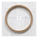 A wooden embroidery hoop shown from above on a white distressed wood background, with a measurement label indicating a diameter of 6.3 inches.