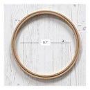 A natural wood embroidery hoop shown on a white wood plank background, with a measurement overlay indicating a diameter of 8.7 inches.