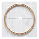 A natural wood embroidery hoop shown on a white wood-textured background, with measurement lines and a label indicating a diameter of 12.2 inches.