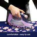 Person using a purple and pink iron on a floral ironing board with 'oliso' branding.