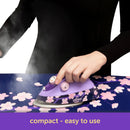 Person ironing fabric with a Oliso Mini Project Iron With Solemate Yaya Han iron on a floral patterned surface.