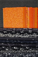 Stack of fabric with orange, black, and white patterns used in the Peek-a-Boo Pumpkin Wall Hanging Quilt Kit.