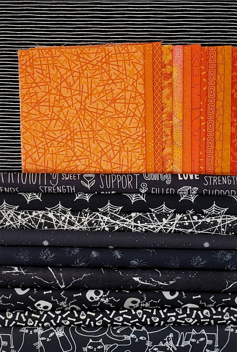 Stack of fabric with orange, black, and white patterns used in the Peek-a-Boo Wall Hanging Quilt Kit.