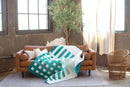 Pattern in "Quilts in Modern Color" shows green and white quilt draped over a brown sofa in a room with large windows and a plant.