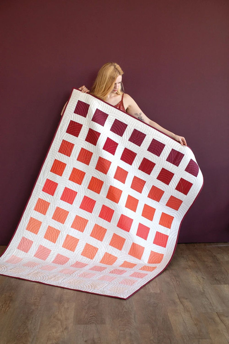 Pattern in "Quilts in Modern Color" shows woman holding a red and orange quilt against a purple wall