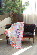 Pattern in "Quilts in Modern Color" shows colorful quilt draped over a dark wooden sofa in a room with a plant and light curtains