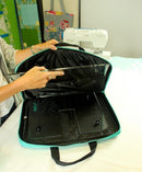 Person holding a black and teal Sew Steady Create Bag with a sewing machine in the background.