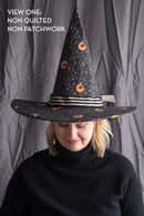 Person wearing a black Spellbound Hat witch hat with against a gray curtain background