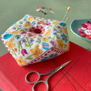 Spring Biscournu Cross Stitch Pattern Colorful embroidered pin cushion with sewing tools on a red surface