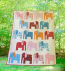 Colorful elephant-patterned quilt called Stomping Ground on a grassy outdoor background